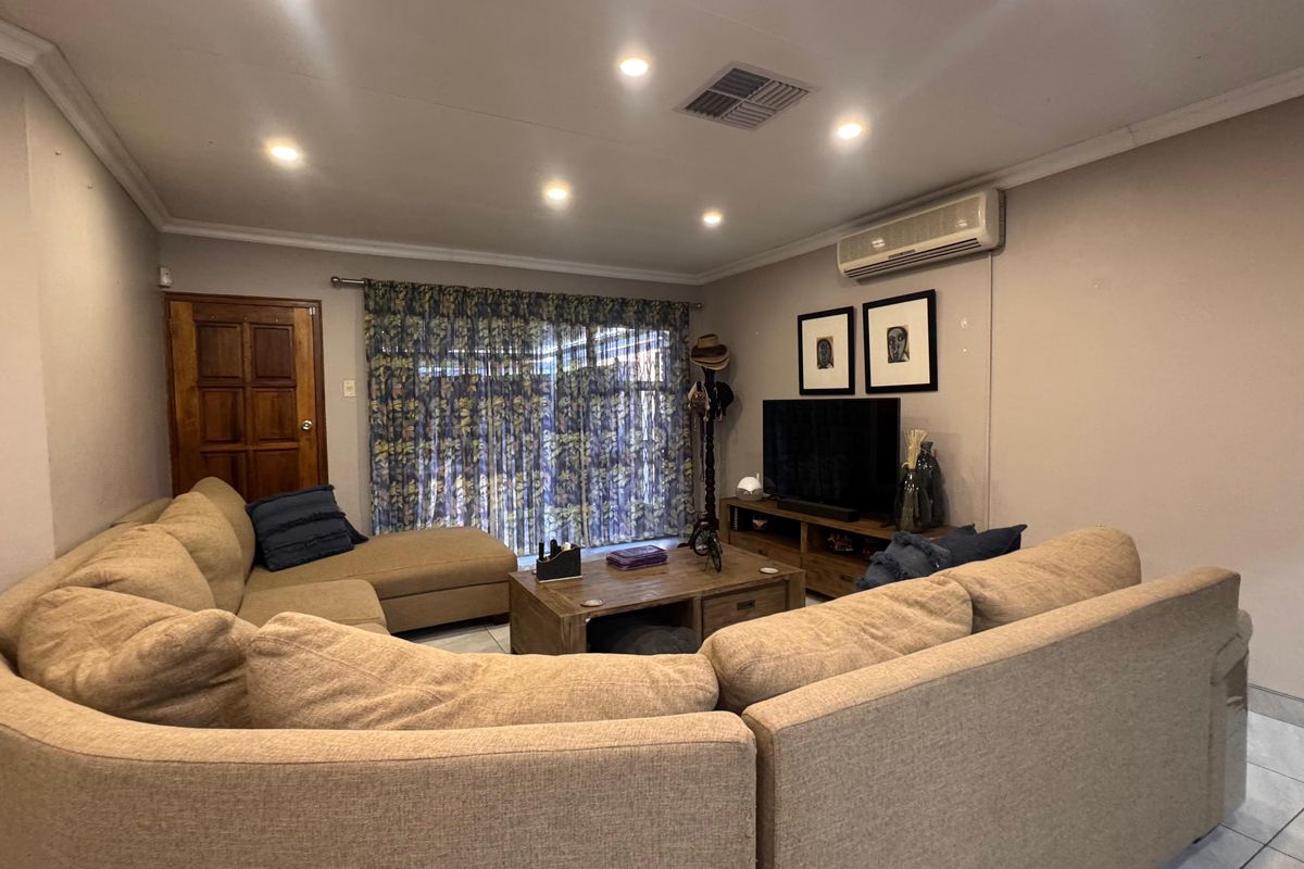 A comfortable living room featuring tiled flooring, recessed downlighting, and an integrated air conditioning unit, with access to the exterior via a sliding glass door.