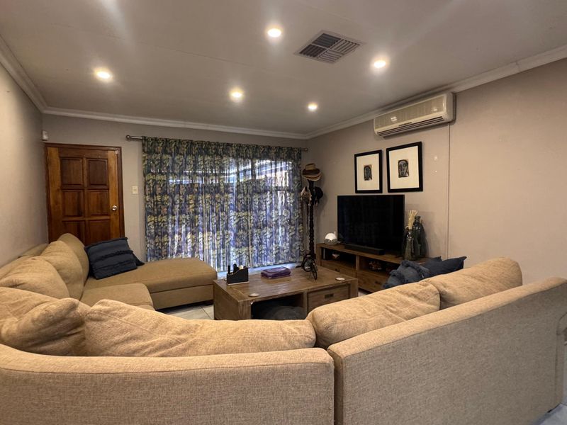 A comfortable living room featuring tiled flooring, recessed downlighting, and an integrated air conditioning unit, with access to the exterior via a sliding glass door.