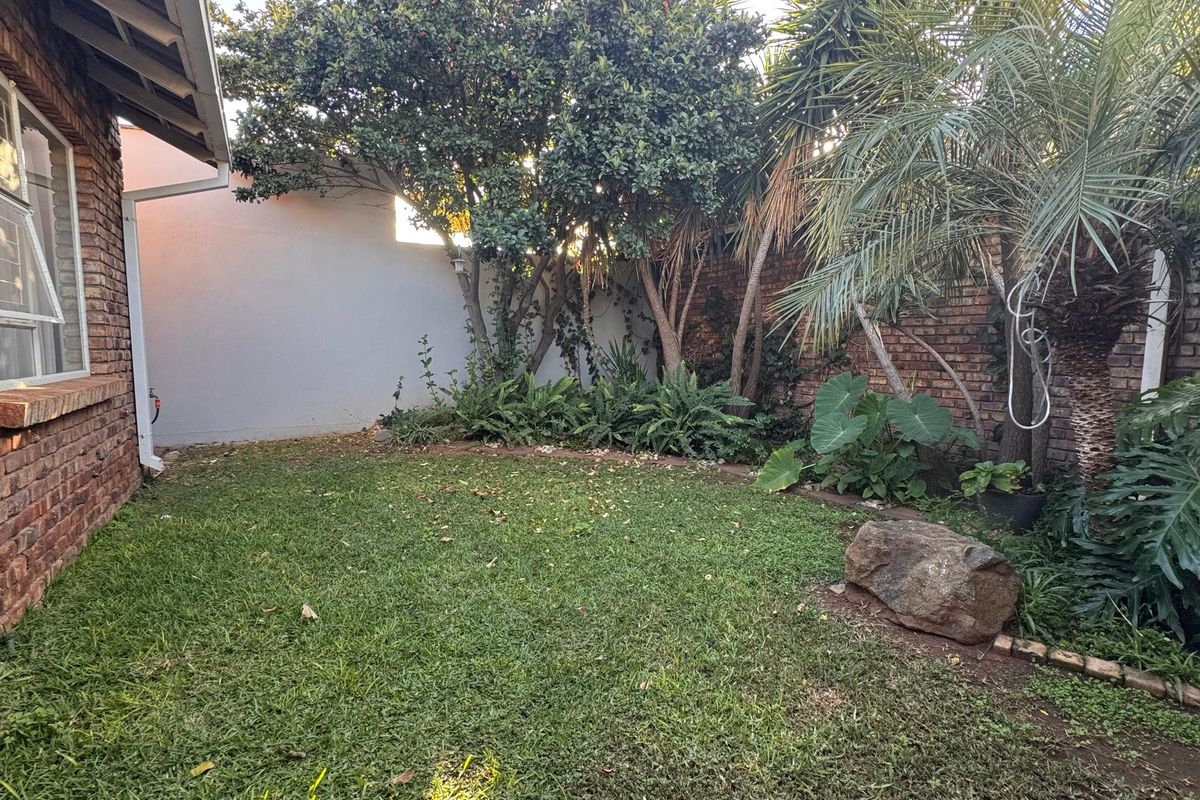 A private rear garden area featuring a well-maintained lawn, established trees, and a brick boundary wall adjacent to the house exterior.