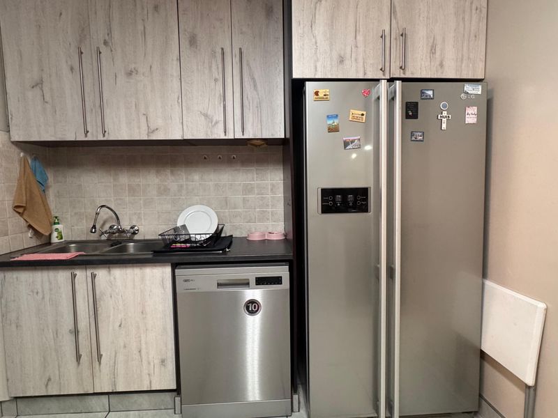 A functional scullery area featuring light wood-grain cabinetry, a double bowl sink with a tiled backsplash, and dedicated space for a dishwasher.