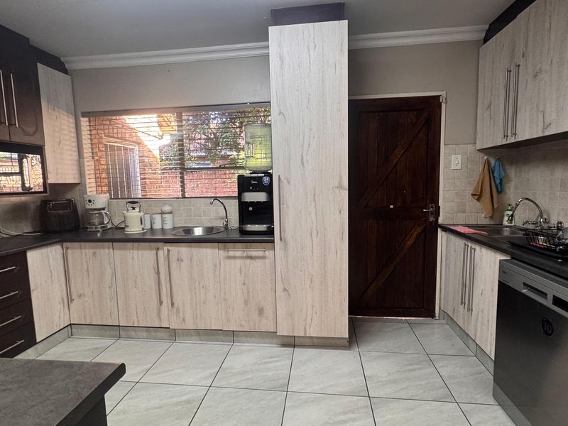 A functional kitchen featuring light wood-grain cabinetry, dark countertops, tiled flooring, and a built-in oven with integrated dishwasher.