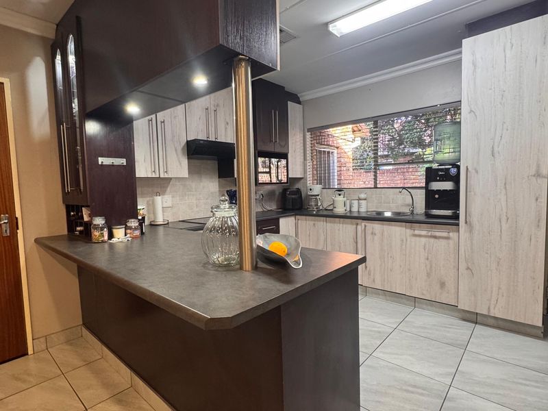 A functional kitchen featuring two-tone cabinetry, dark laminate countertops, a breakfast bar, and tiled flooring with ample storage space.