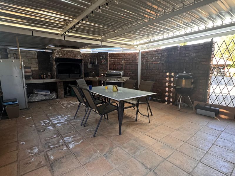 Covered outdoor patio featuring a built-in braai, exposed brick walls, and tiled flooring, providing a functional space for outdoor dining and entertainment.