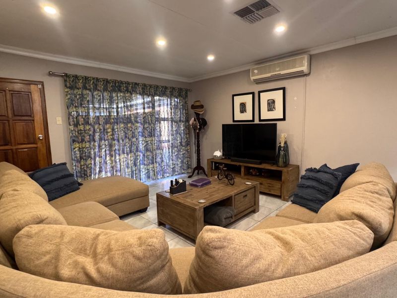 A comfortable living room featuring tiled flooring, recessed downlighting, and a wall-mounted split-system air conditioner, with access to the exterior via a sliding glass door.