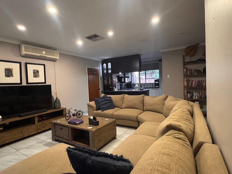 An open-plan living area featuring tiled flooring, recessed lighting, and a split-system air conditioner, seamlessly flowing into a functional kitchen space.