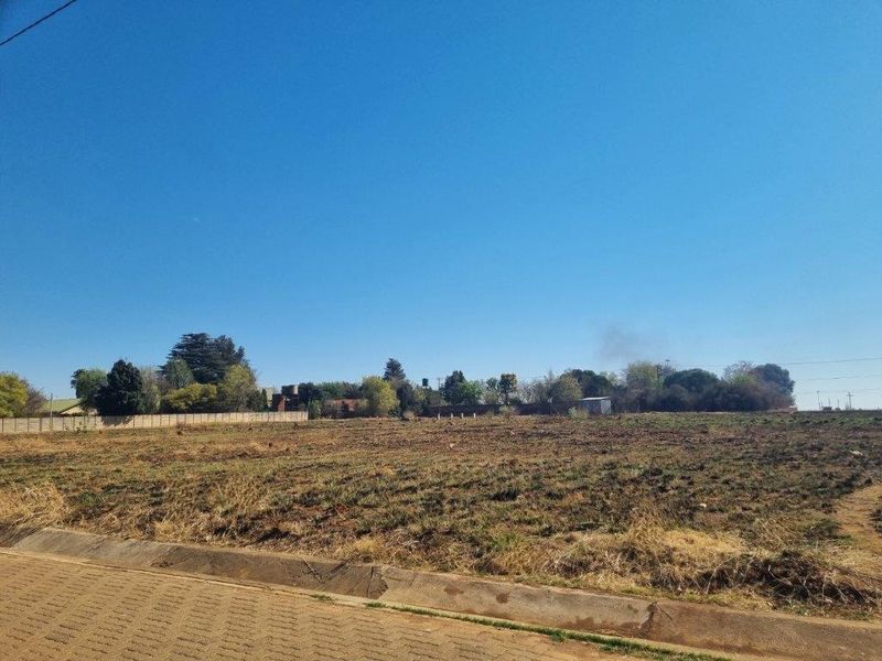 A vacant residential plot featuring a concrete boundary wall and paved curb, offering a clear space for future development.