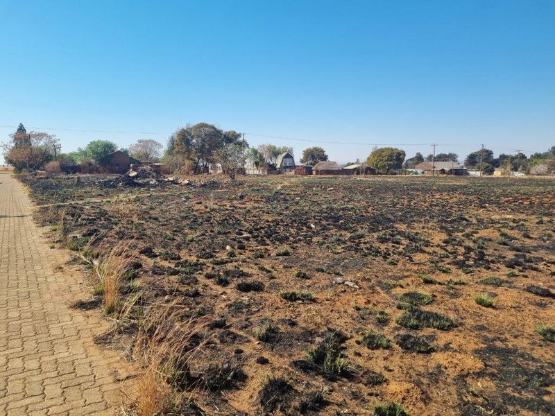 A vacant residential plot featuring a paved driveway access point, showing signs of recent fire damage to the ground cover.