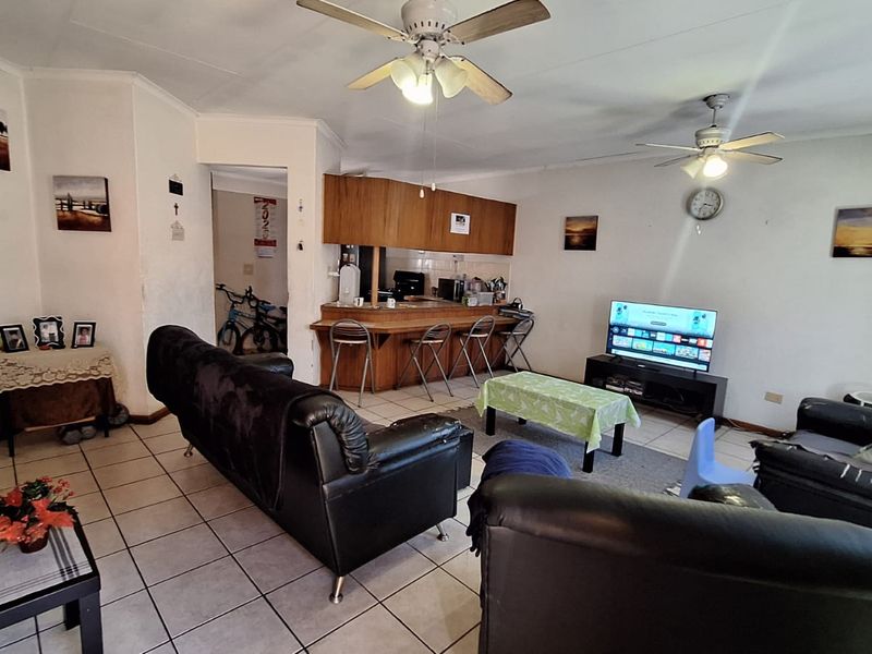 Open-plan living area featuring tiled flooring, dual ceiling fans, and a breakfast bar with built-in cabinetry, offering a functional layout for daily living.