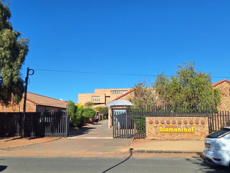 Front entrance view of the Diamanthof townhouse complex, featuring a brick boundary wall, secure metal gate, and paved driveway access.