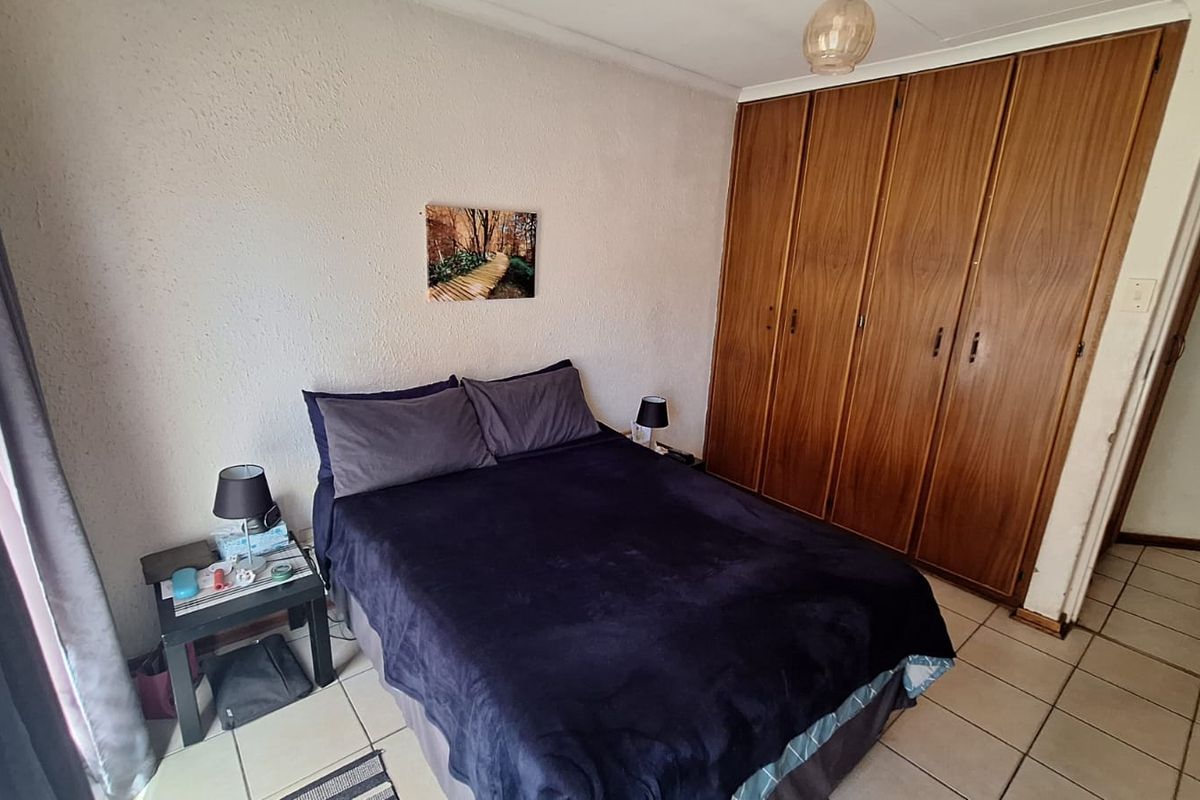 A functional bedroom featuring built-in wooden cupboards, tiled flooring, and textured walls, offering a practical layout with standard storage solutions.
