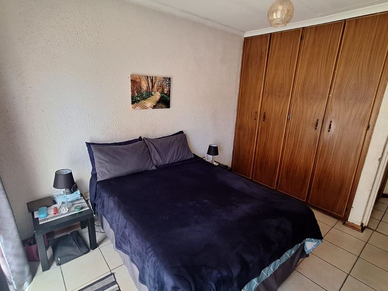 A functional bedroom featuring built-in wooden cupboards, tiled flooring, and textured walls, offering a practical layout with standard storage solutions.