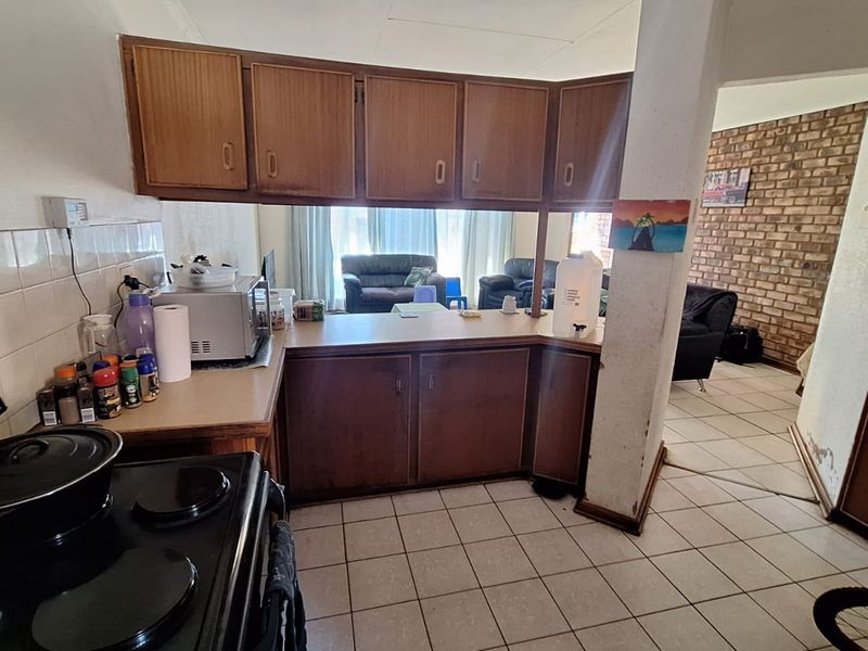 Open plan kitchen and living area featuring dated wooden cabinetry, tiled flooring, and an exposed brick wall, offering potential for modern renovation.
