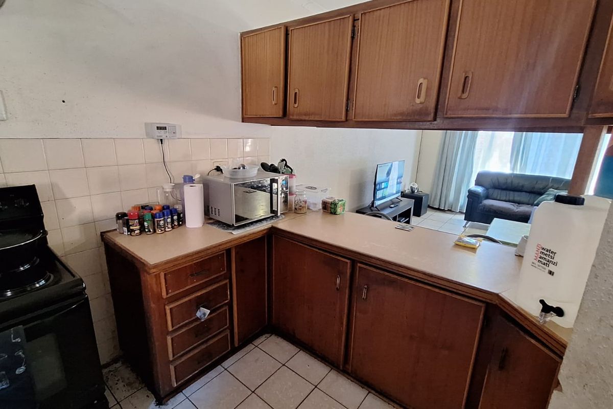 A dated kitchen featuring wood-look cabinetry, laminate countertops, and tiled flooring, offering potential for a modern renovation to enhance the space.