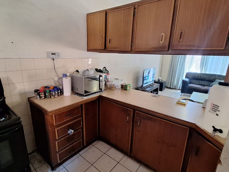 A dated kitchen featuring wood-look cabinetry, laminate countertops, and tiled flooring, offering potential for a modern renovation to enhance the space.