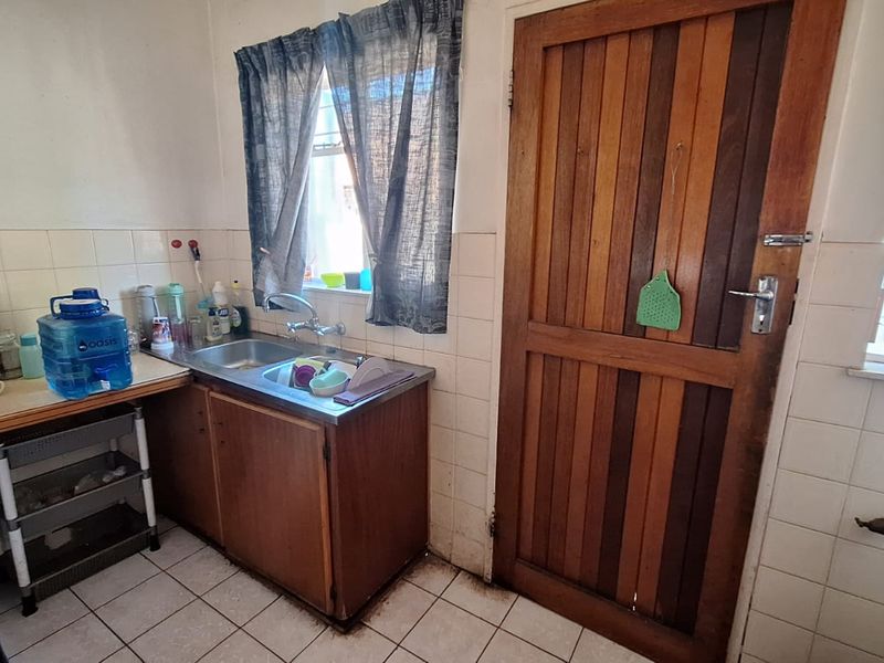 A compact kitchen area featuring a stainless steel sink, tiled splashback, and wooden cabinetry, providing a functional but dated workspace.