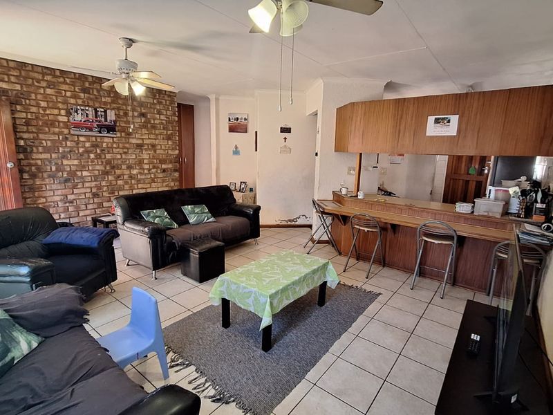 Open-plan living area featuring an exposed brick wall, breakfast bar with built-in cabinetry, and tiled flooring throughout.