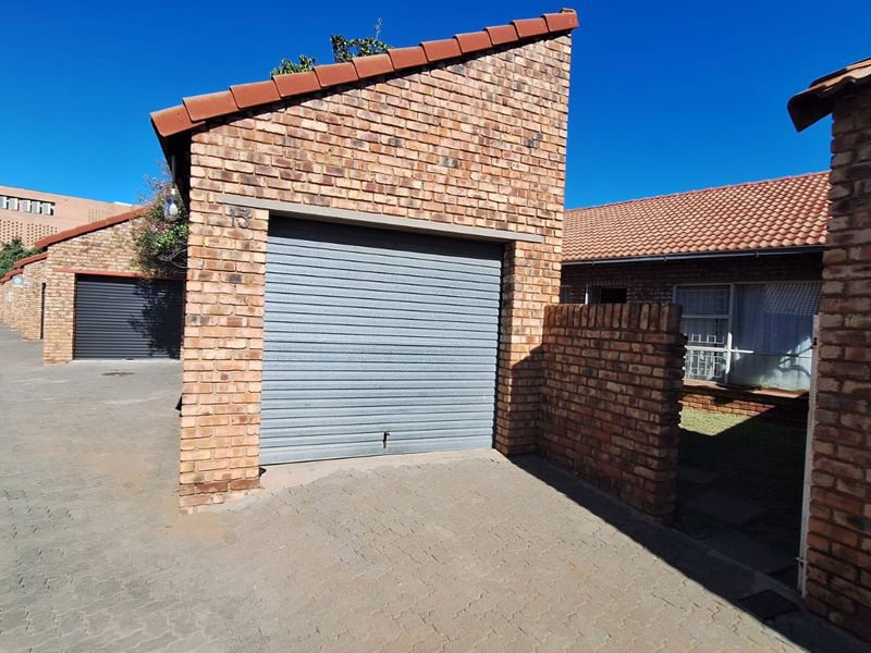 A view of a face brick townhouse garage featuring a secure roller shutter door and paved driveway access.