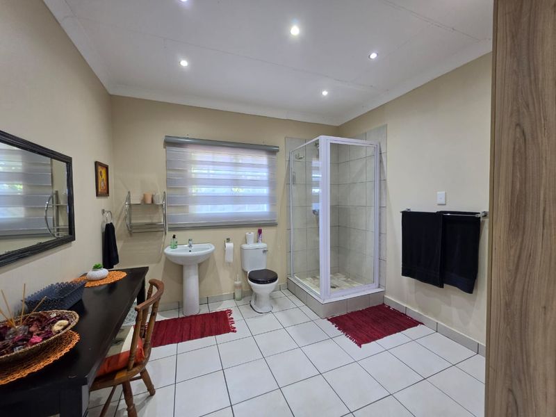 A functional bathroom featuring a pedestal washbasin, a toilet, and a glass-enclosed shower with tiled flooring and recessed lighting.