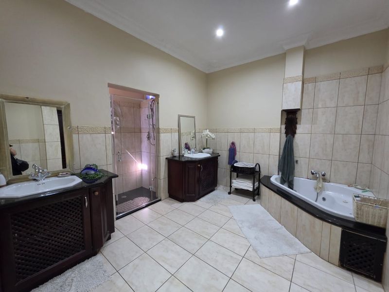 Spacious bathroom featuring dual built-in vanities, a drop-in bathtub, and a separate glass-enclosed shower with neutral ceramic tiling throughout.