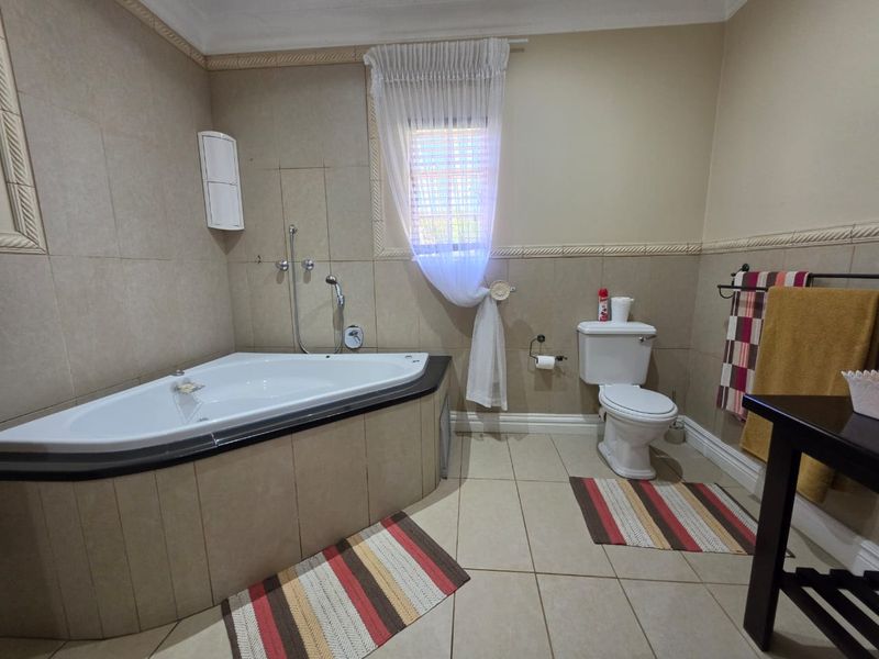 A functional bathroom featuring a corner bathtub, ceramic wall and floor tiling, and standard sanitary fixtures with decorative wall molding.