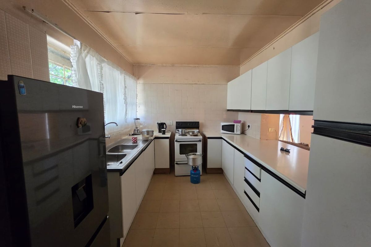A functional kitchen featuring white cabinetry, a double basin sink, and a freestanding stove, requiring cosmetic updates to the ceiling and finishes.