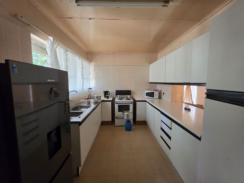 A functional kitchen featuring white cabinetry, a double basin sink, and a freestanding stove, requiring cosmetic updates to the ceiling and finishes.