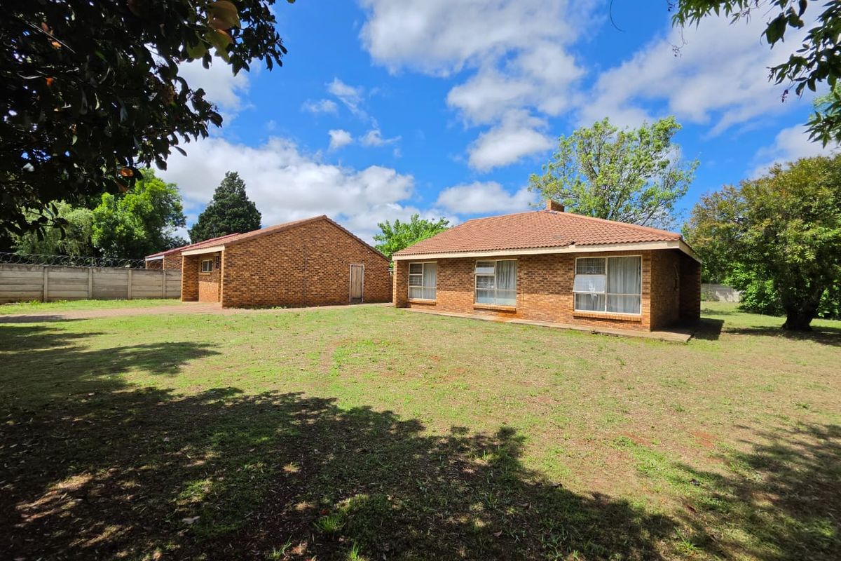 A view of the rear of the property featuring a face brick house with a tiled roof and a spacious garden area.