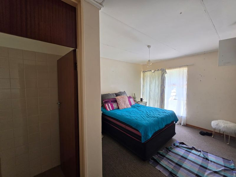 Bedroom featuring carpeted flooring, a built-in cupboard, and an adjacent tiled shower area, requiring cosmetic updates to the walls and ceiling.