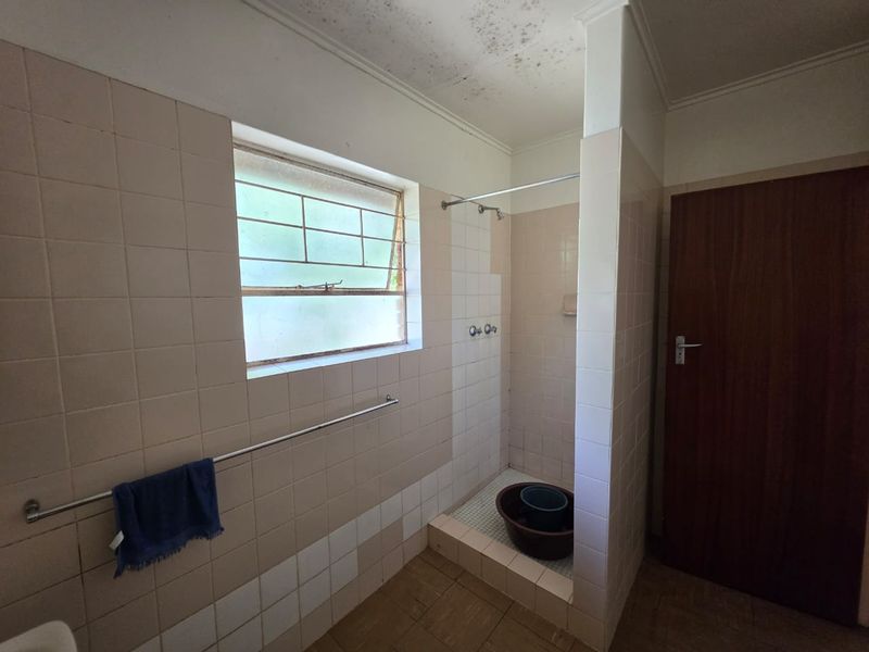 A dated bathroom featuring a tiled shower enclosure and window with security bars, currently requiring maintenance and cosmetic updates to the ceiling and tiling.