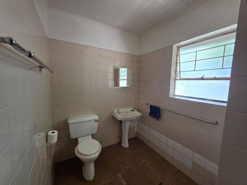 A dated bathroom featuring a pedestal basin, toilet, and tiled finishes, offering a blank canvas for renovation and modernization.