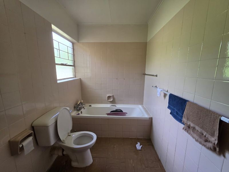 A dated bathroom featuring a built-in bathtub, toilet, and full-height wall tiling. The space is ready for a modern renovation.