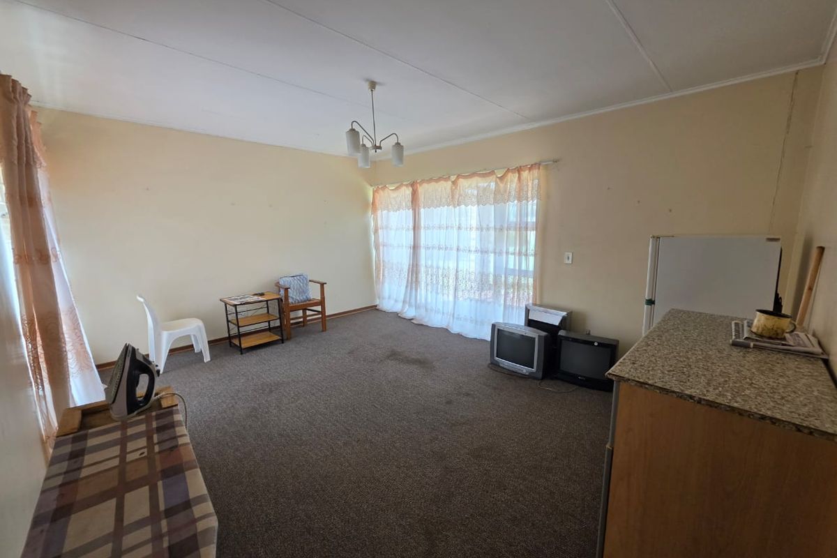 A spacious living area featuring carpeted flooring and a neutral color palette, offering a blank canvas for potential renovation and modernization.