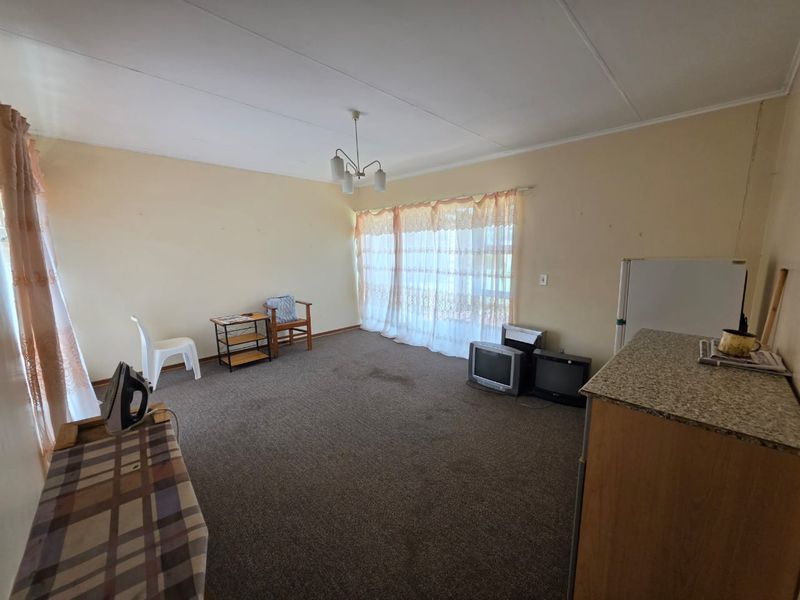 A spacious living area featuring carpeted flooring and a neutral color palette, offering a blank canvas for potential renovation and modernization.