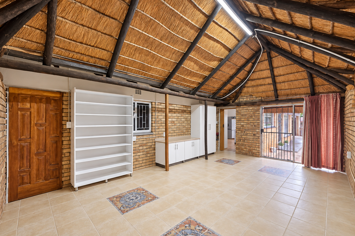 Spacious living area featuring a high thatched roof with exposed timber rafters, exposed brick walls, and tiled flooring with decorative inlays.