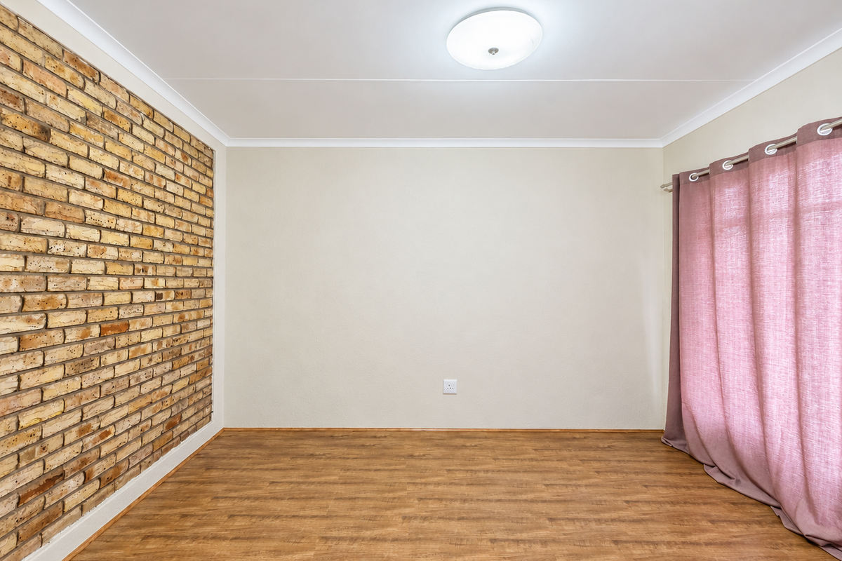 An empty bedroom featuring a rustic exposed brick feature wall, warm-toned laminate flooring, and neutral painted walls.