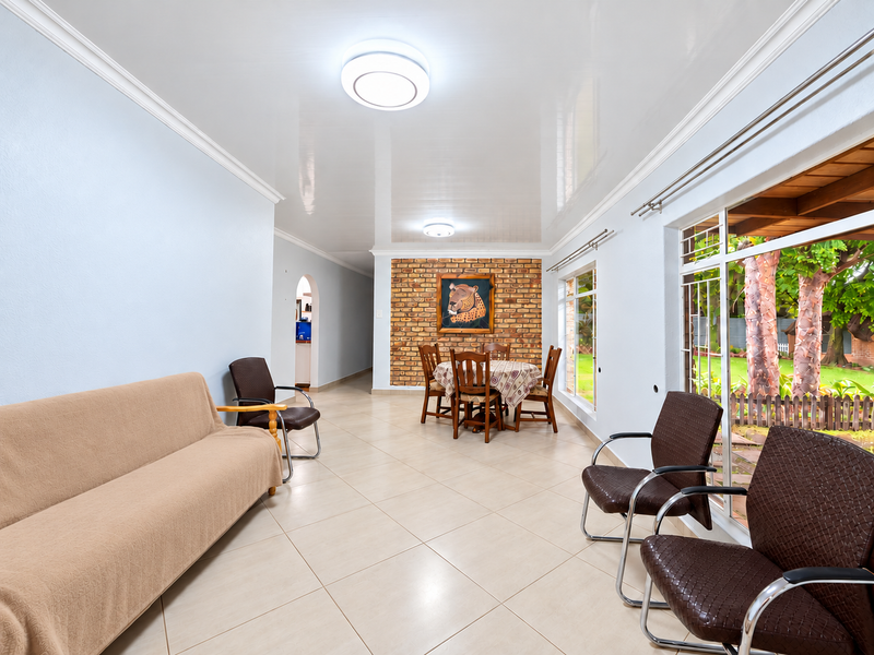 Spacious open-plan living and dining area featuring a striking exposed brick feature wall, glossy ceiling, and large windows overlooking the garden.