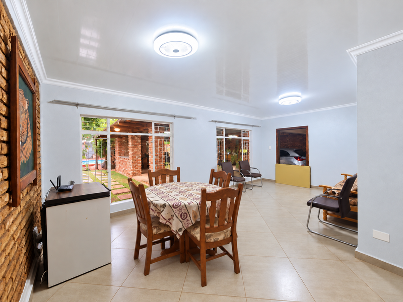 Spacious open-plan living area featuring tiled flooring, an exposed brick feature wall, and large windows providing natural light and views of the outdoor area.