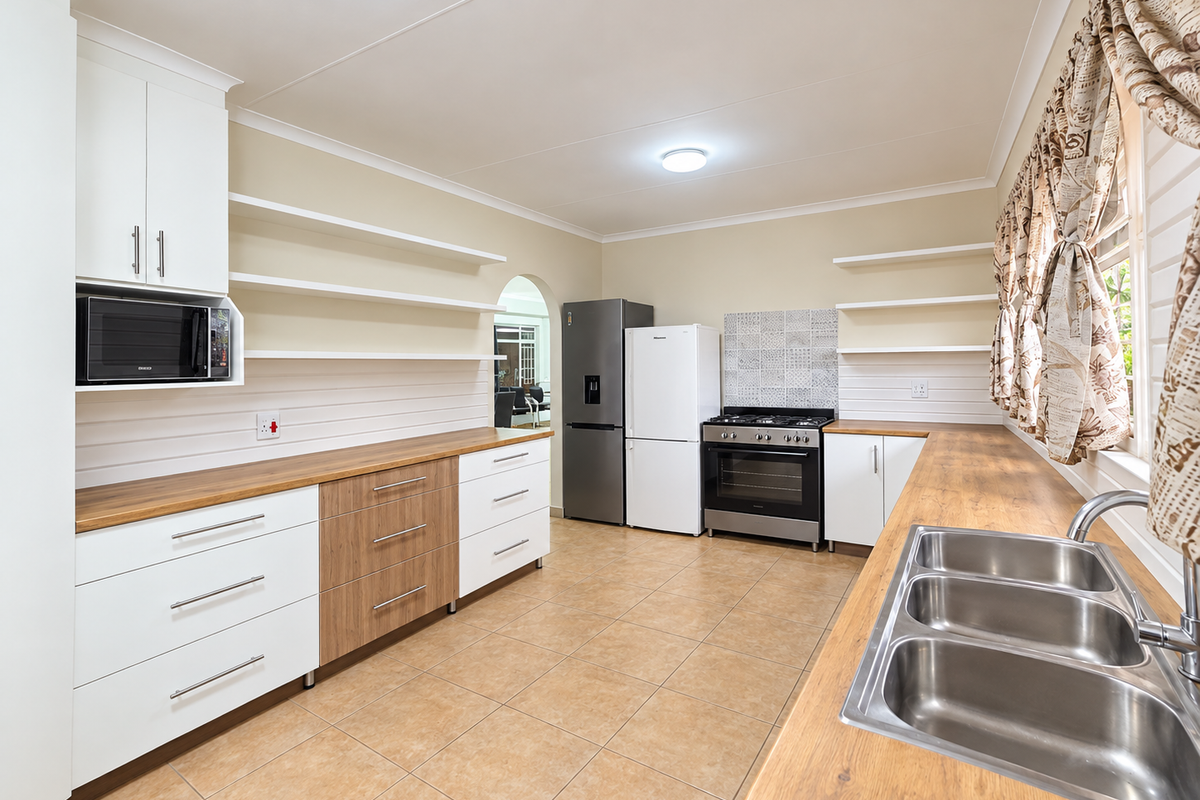A well-maintained kitchen featuring modern white and wood-tone cabinetry, wooden countertops, a stainless steel double sink, and a gas stove with tiled splashback.