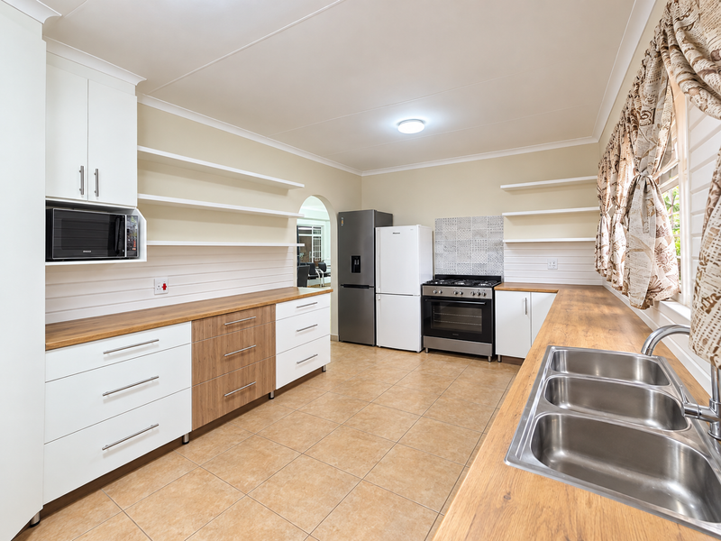 A well-maintained kitchen featuring modern white and wood-tone cabinetry, wooden countertops, a stainless steel double sink, and a gas stove with tiled splashback.