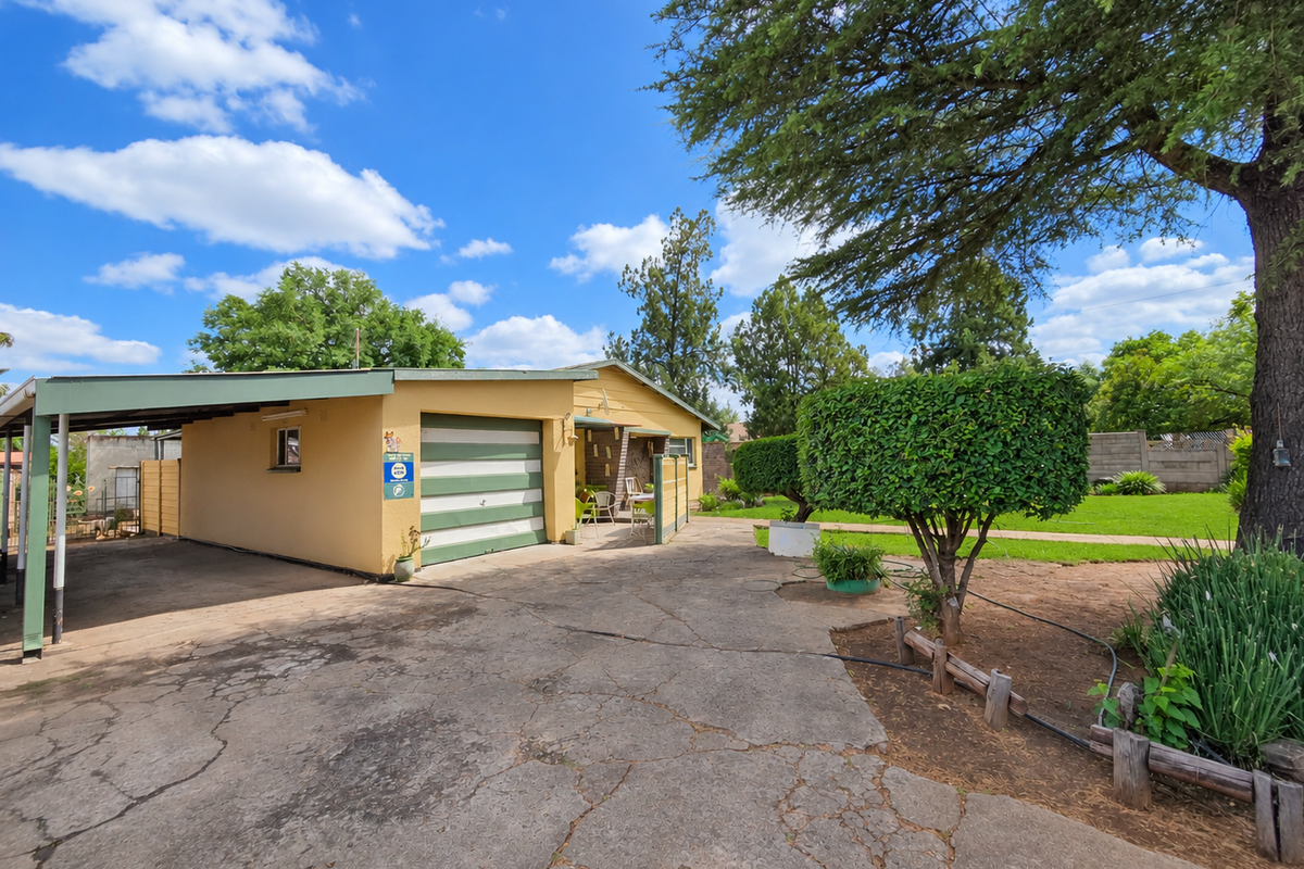 Front view of the property featuring a carport, garage, and a spacious driveway set within a landscaped garden area.