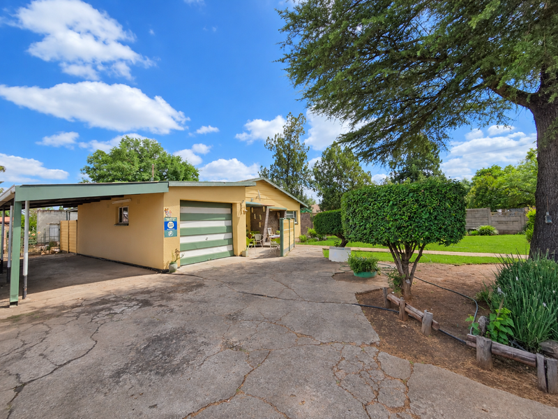 Front view of the property featuring a carport, garage, and a spacious driveway set within a landscaped garden area.