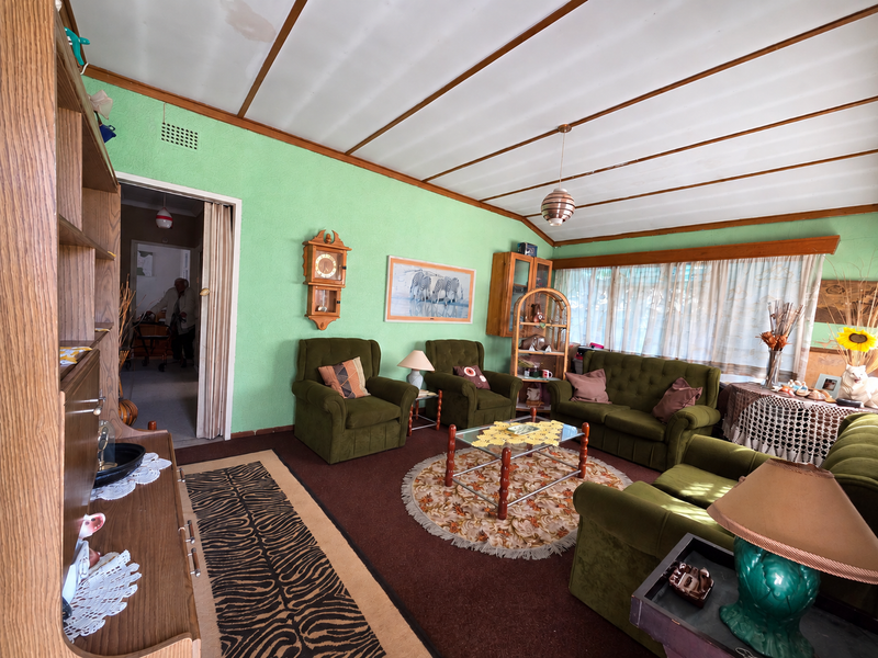 A dated living room featuring textured green walls, exposed beam ceilings, and a folding door leading to an adjacent space.