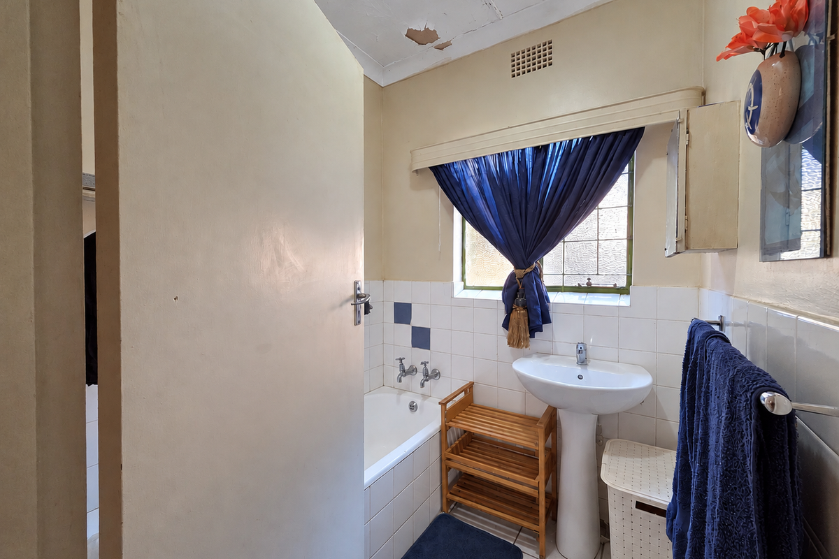 A compact bathroom featuring a pedestal basin, built-in bathtub, and tiled splashback, currently requiring ceiling repairs and cosmetic updates.