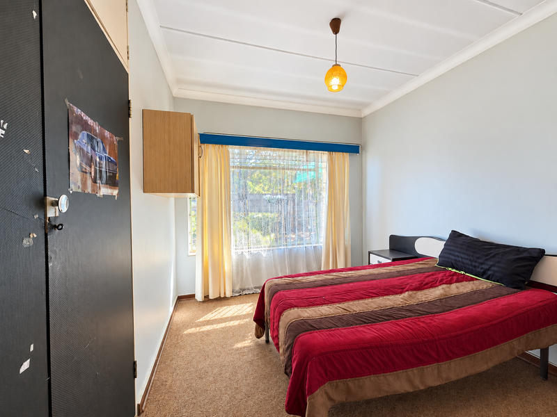 A functional bedroom featuring built-in cupboard storage, carpeted flooring, and natural light through a large window.