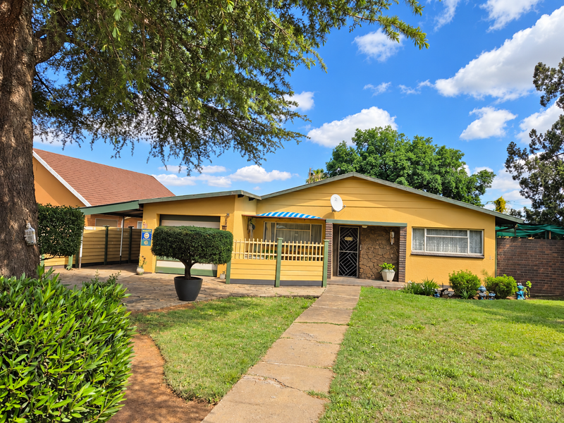 Front view of a single-story house featuring a paved driveway, carport, stone-clad entrance, and a well-maintained front garden with a concrete walkway.