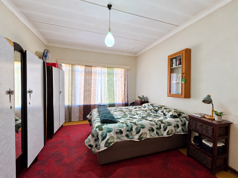 A bedroom featuring a built-in wardrobe, wall-mounted cabinet, and pendant lighting. The room shows signs of wear, including ceiling staining and dated carpet flooring.