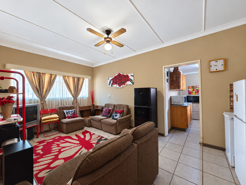 Open plan living area featuring tiled floors and a ceiling fan, with an adjacent kitchen area visible through the doorway.
