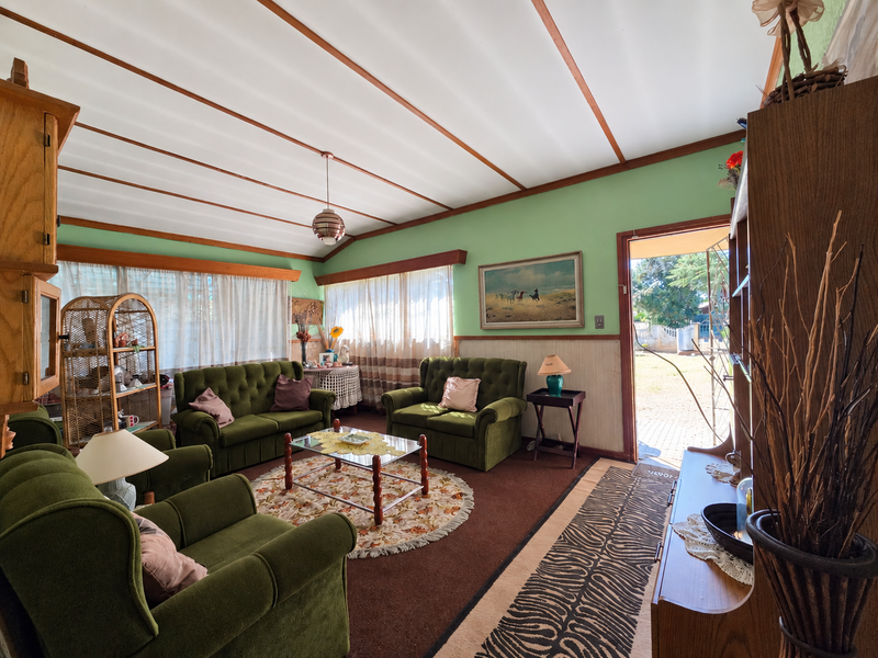 A dated living room featuring exposed beam ceilings, wainscoting, and direct access to the exterior, offering potential for a modern renovation.