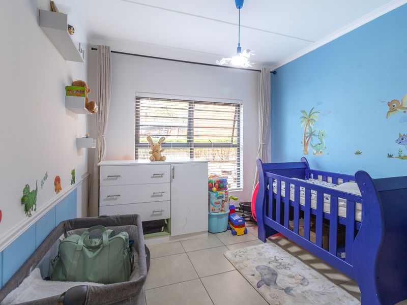 A bedroom featuring tiled flooring, a window with horizontal blinds, and wall-mounted shelving, currently utilized as a nursery.