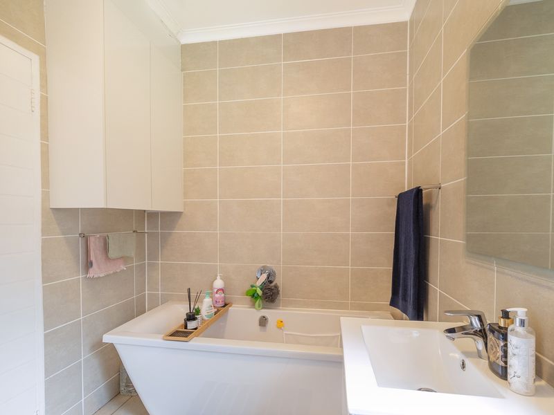A modern bathroom featuring neutral wall tiles, a built-in bathtub, a sleek basin with a mixer tap, and ample wall-mounted storage cabinetry.